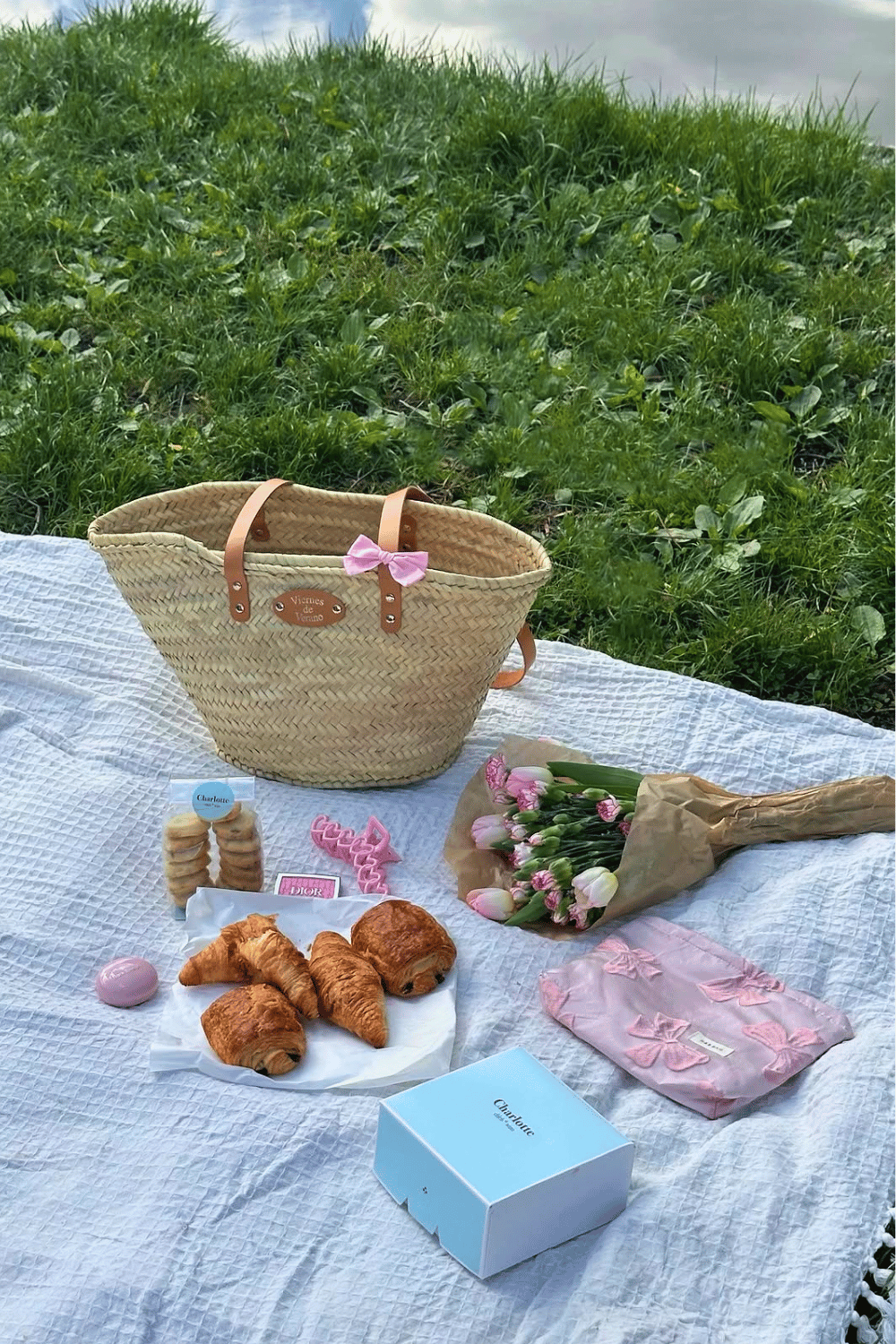 Cozy galentine’s picnic setup with basket, pastries, and flowers on blanket