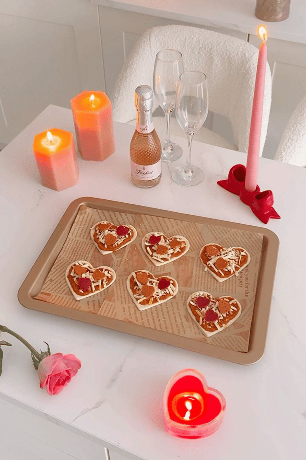 Heart-shaped galentine’s snacks on a tray with candles and sparkling wine
