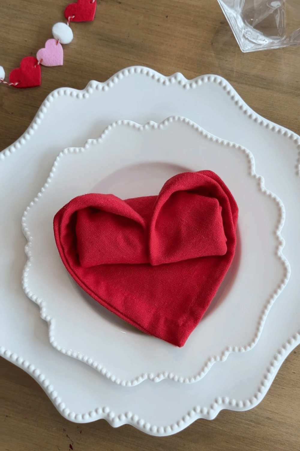 Galentine’s place setting with red heart-shaped napkin folded on white dinner plates