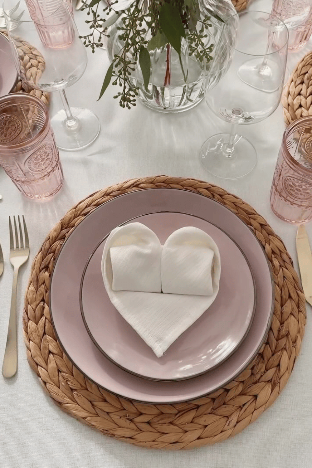 Soft pink Galentine’s place setting with heart napkin fold and woven placemat